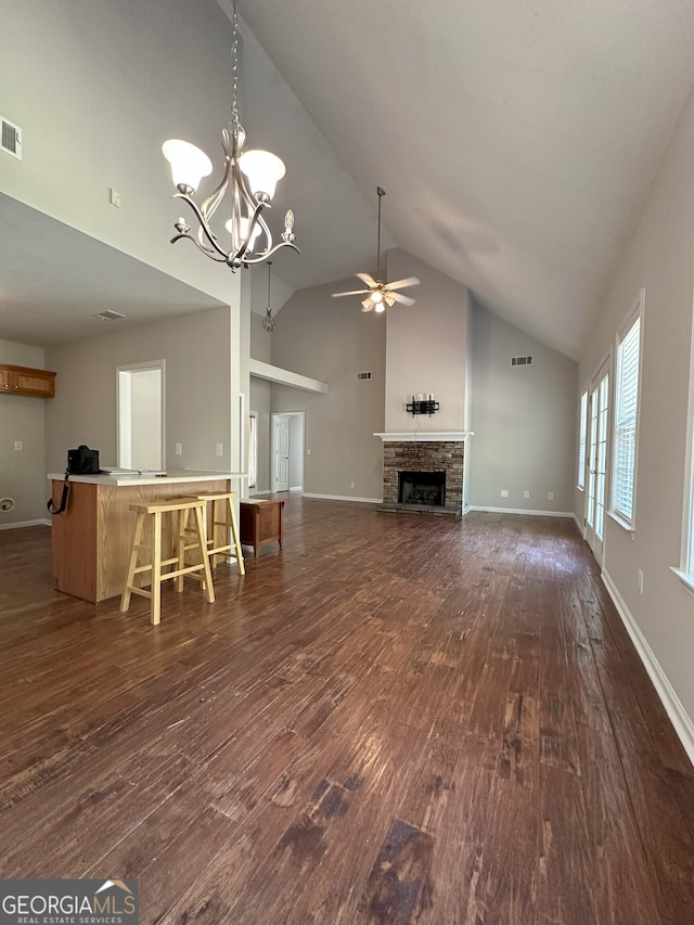 unfurnished living room featuring ceiling fan with notable chandelier, a stone fireplace, lofted ceiling, and dark wood-type flooring