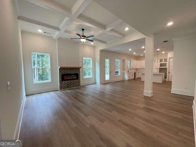 unfurnished living room featuring coffered ceiling, ceiling fan, dark wood-type flooring, sink, and beam ceiling