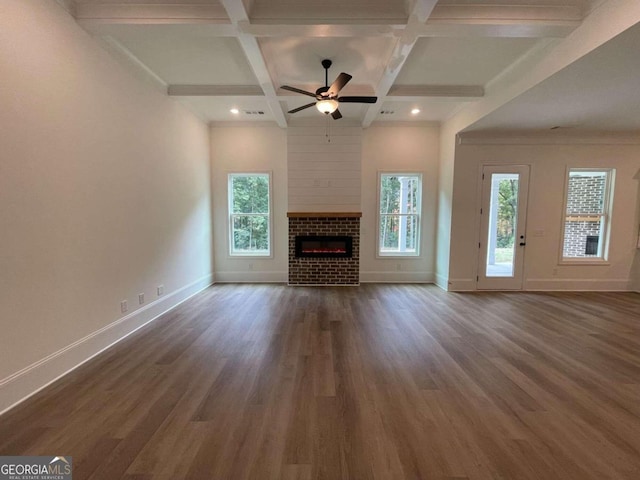 unfurnished living room featuring a healthy amount of sunlight, a brick fireplace, ceiling fan, and dark wood-type flooring