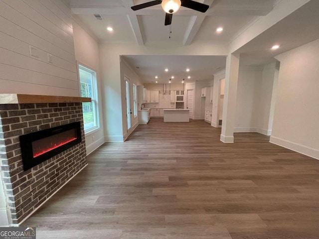 unfurnished living room with a fireplace, ceiling fan, dark hardwood / wood-style flooring, and beamed ceiling