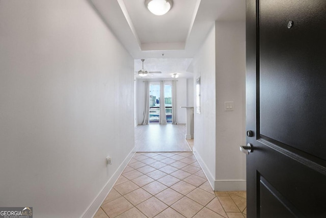 hall with light tile patterned floors and a tray ceiling