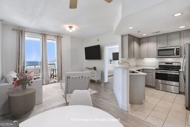 kitchen with gray cabinetry, sink, appliances with stainless steel finishes, light hardwood / wood-style floors, and kitchen peninsula