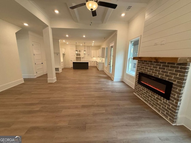 unfurnished living room with beam ceiling, ceiling fan, a brick fireplace, dark hardwood / wood-style flooring, and crown molding