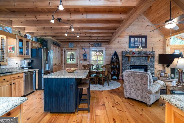 kitchen featuring light stone countertops, a kitchen breakfast bar, stainless steel appliances, wooden walls, and light hardwood / wood-style flooring