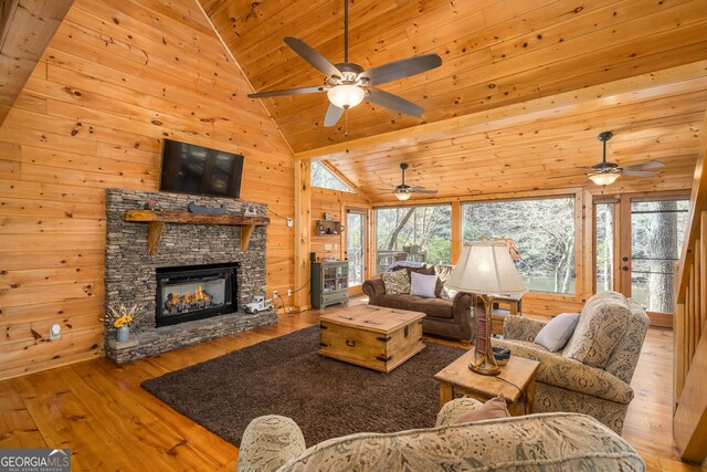 living room with wood ceiling, a stone fireplace, wooden walls, and light hardwood / wood-style floors