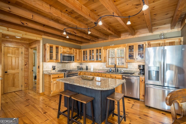 kitchen with a kitchen island, light stone countertops, stainless steel appliances, and light hardwood / wood-style flooring