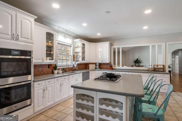 kitchen with appliances with stainless steel finishes, ornamental molding, sink, light tile patterned floors, and white cabinets