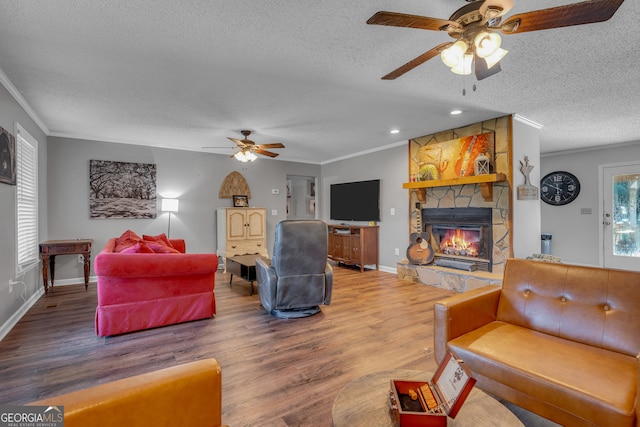 living room featuring ornamental molding, a textured ceiling, ceiling fan, a fireplace, and hardwood / wood-style floors