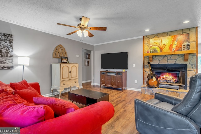 living room featuring a textured ceiling, ceiling fan, crown molding, wood-type flooring, and a fireplace