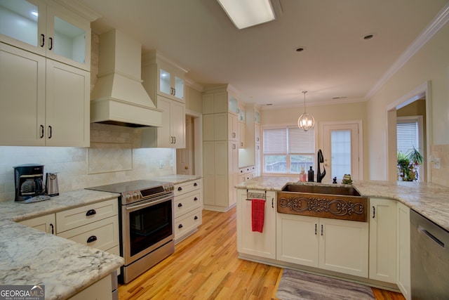 kitchen with light stone countertops, hanging light fixtures, stainless steel appliances, premium range hood, and light hardwood / wood-style floors