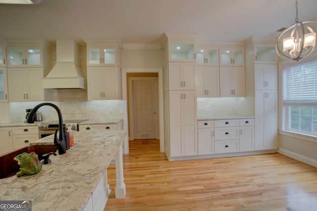 kitchen featuring custom range hood, tasteful backsplash, light hardwood / wood-style flooring, and pendant lighting