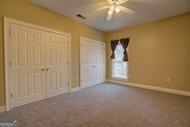 unfurnished bedroom with ceiling fan, carpet floors, and multiple closets