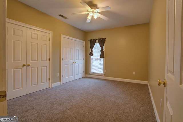 unfurnished bedroom with carpet flooring, ceiling fan, and two closets