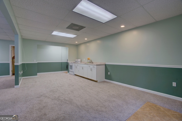 basement featuring a paneled ceiling, sink, and light colored carpet