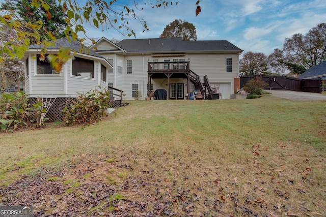 rear view of property featuring a garage, a wooden deck, and a lawn