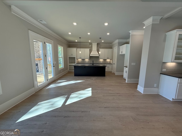 kitchen featuring sink, tasteful backsplash, premium range hood, a kitchen island with sink, and white cabinets