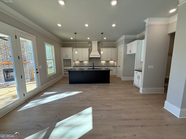 kitchen with tasteful backsplash, an island with sink, light hardwood / wood-style floors, white cabinets, and custom range hood