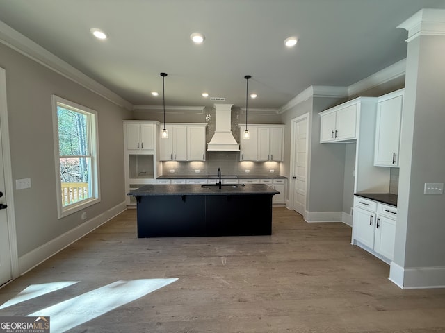 kitchen featuring white cabinetry, hanging light fixtures, light hardwood / wood-style flooring, a kitchen island with sink, and custom exhaust hood