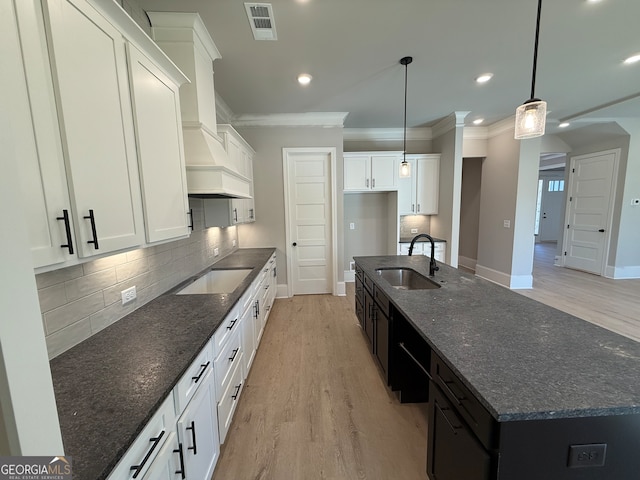 kitchen with pendant lighting, dark stone countertops, sink, and an island with sink