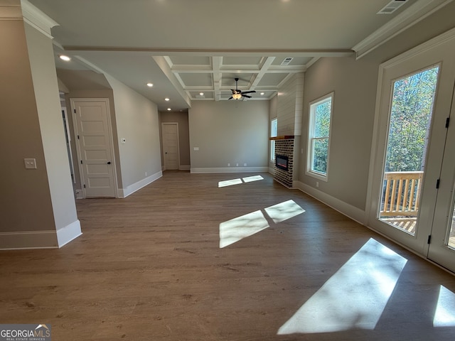 spare room featuring light wood-type flooring, a brick fireplace, ornamental molding, coffered ceiling, and ceiling fan