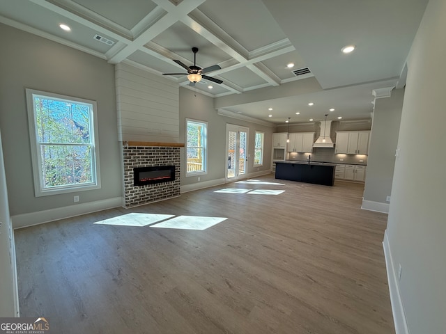 unfurnished living room with coffered ceiling, a brick fireplace, ceiling fan, beam ceiling, and light hardwood / wood-style floors