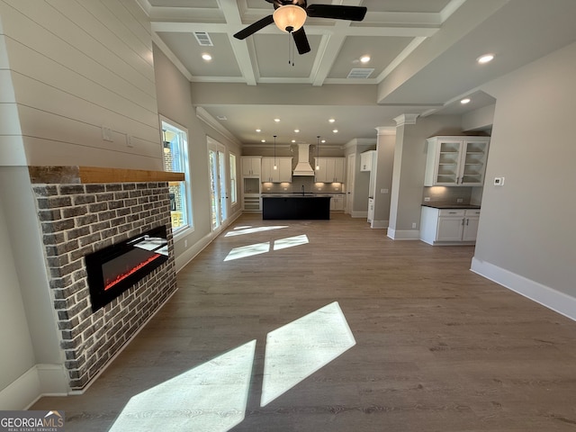 unfurnished living room featuring a brick fireplace, dark hardwood / wood-style floors, ceiling fan, beamed ceiling, and decorative columns