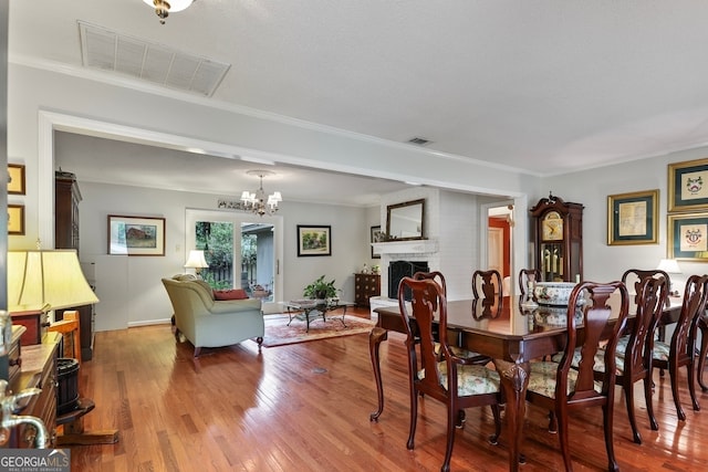 dining space with crown molding, a textured ceiling, a fireplace, wood-type flooring, and a chandelier