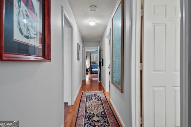 hall with a textured ceiling and light hardwood / wood-style flooring