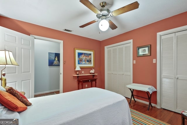 bedroom featuring ceiling fan, dark wood-type flooring, and multiple closets