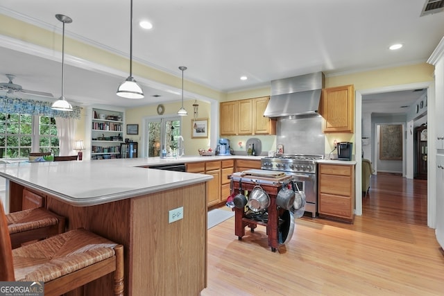 kitchen with high end stainless steel range oven, wall chimney range hood, a kitchen breakfast bar, kitchen peninsula, and light hardwood / wood-style floors