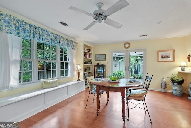 dining space with ceiling fan, built in features, ornamental molding, and light wood-type flooring