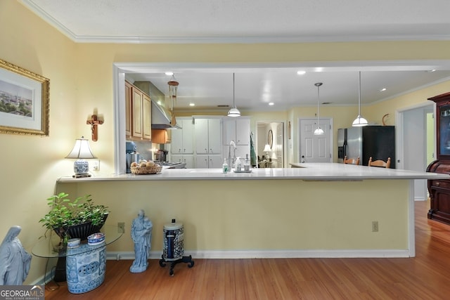 kitchen with kitchen peninsula, light hardwood / wood-style floors, decorative light fixtures, appliances with stainless steel finishes, and ornamental molding