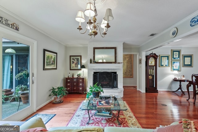 living room featuring hardwood / wood-style floors, a brick fireplace, ornamental molding, and a notable chandelier