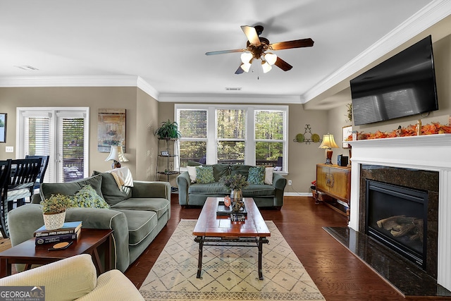 living room with a high end fireplace, crown molding, ceiling fan, and dark wood-type flooring