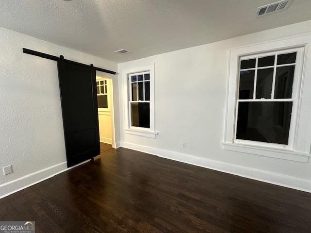 unfurnished room with dark wood-type flooring, a barn door, and a textured ceiling