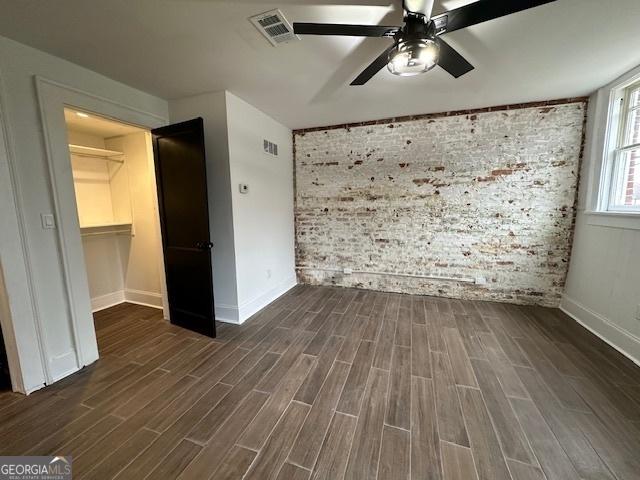 unfurnished bedroom featuring brick wall, dark hardwood / wood-style flooring, a spacious closet, ceiling fan, and a closet