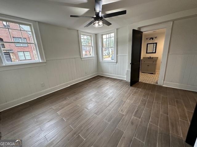 unfurnished bedroom with multiple windows, ensuite bath, dark hardwood / wood-style flooring, and ceiling fan