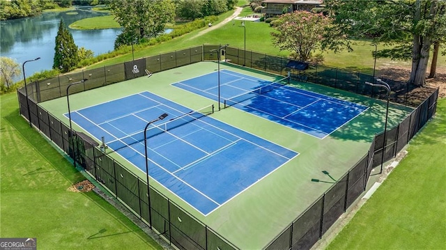 view of tennis court featuring a lawn and a water view