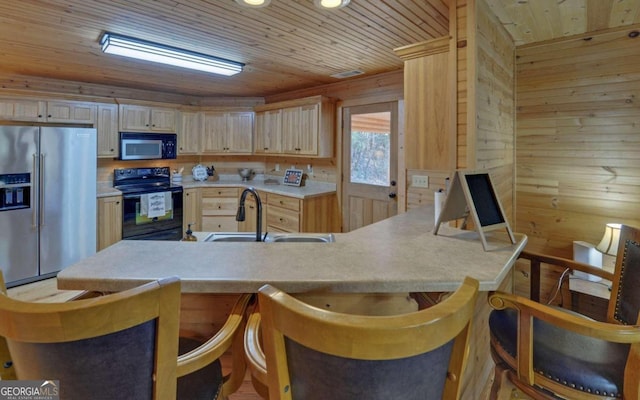 kitchen with kitchen peninsula, wood walls, light brown cabinets, and black appliances