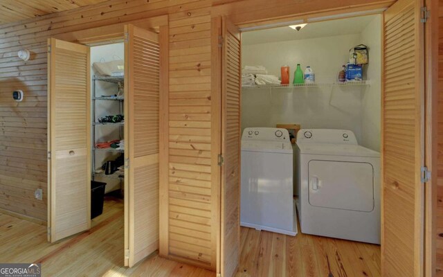 washroom with washing machine and clothes dryer, wooden walls, and light hardwood / wood-style floors