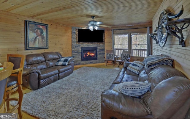 living room featuring ceiling fan, wood walls, a stone fireplace, and wood ceiling