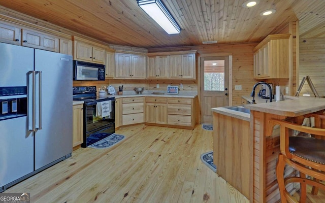 kitchen featuring light brown cabinetry, sink, black appliances, light hardwood / wood-style flooring, and wood walls