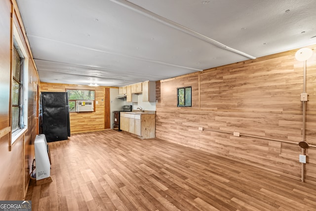 unfurnished living room with light wood-type flooring, wooden walls, and sink