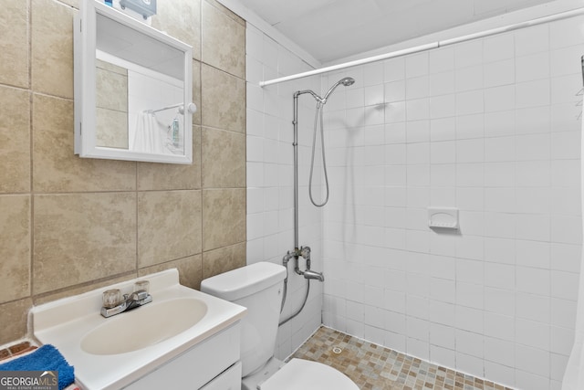 bathroom with a tile shower, vanity, toilet, and tile walls