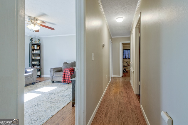 hall featuring a textured ceiling, light wood-type flooring, and crown molding