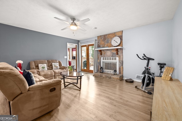 living room featuring a stone fireplace, ceiling fan, a textured ceiling, and hardwood / wood-style flooring