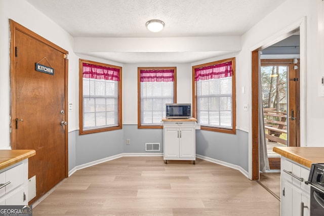 kitchen featuring light hardwood / wood-style flooring, white cabinets, stove, and a textured ceiling