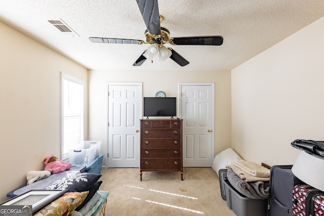 bedroom with ceiling fan, light carpet, and a textured ceiling