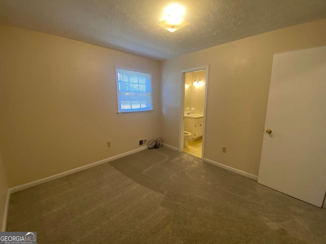 unfurnished bedroom featuring carpet flooring, ensuite bathroom, sink, and a textured ceiling