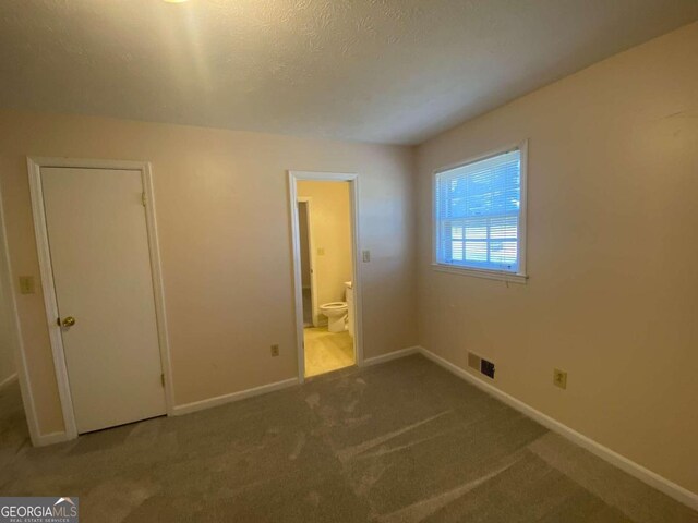 unfurnished bedroom with ensuite bathroom, carpet floors, a textured ceiling, and a closet